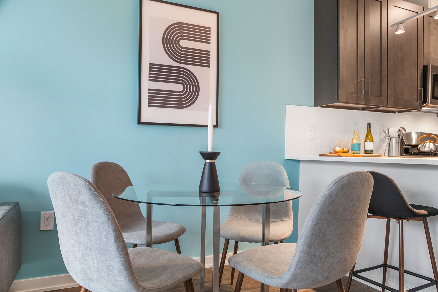 Detail of eat in glass table with 4 chairs near kitchen, light teal accent wall and wood floors