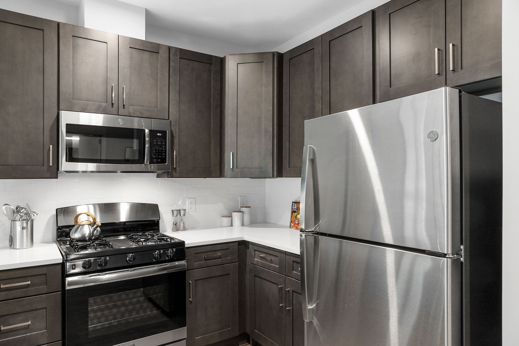 Corner of kitchen with with dark cabinetry, light counters and stainless steel appliances